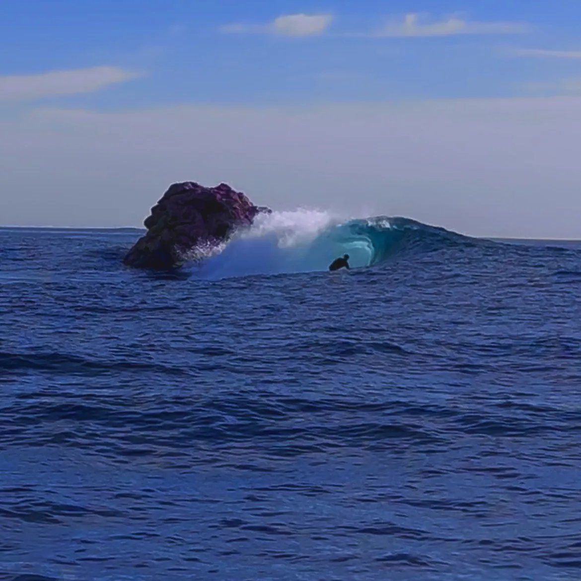 Surfeur dans une vague derrière un rocher, mer bleue