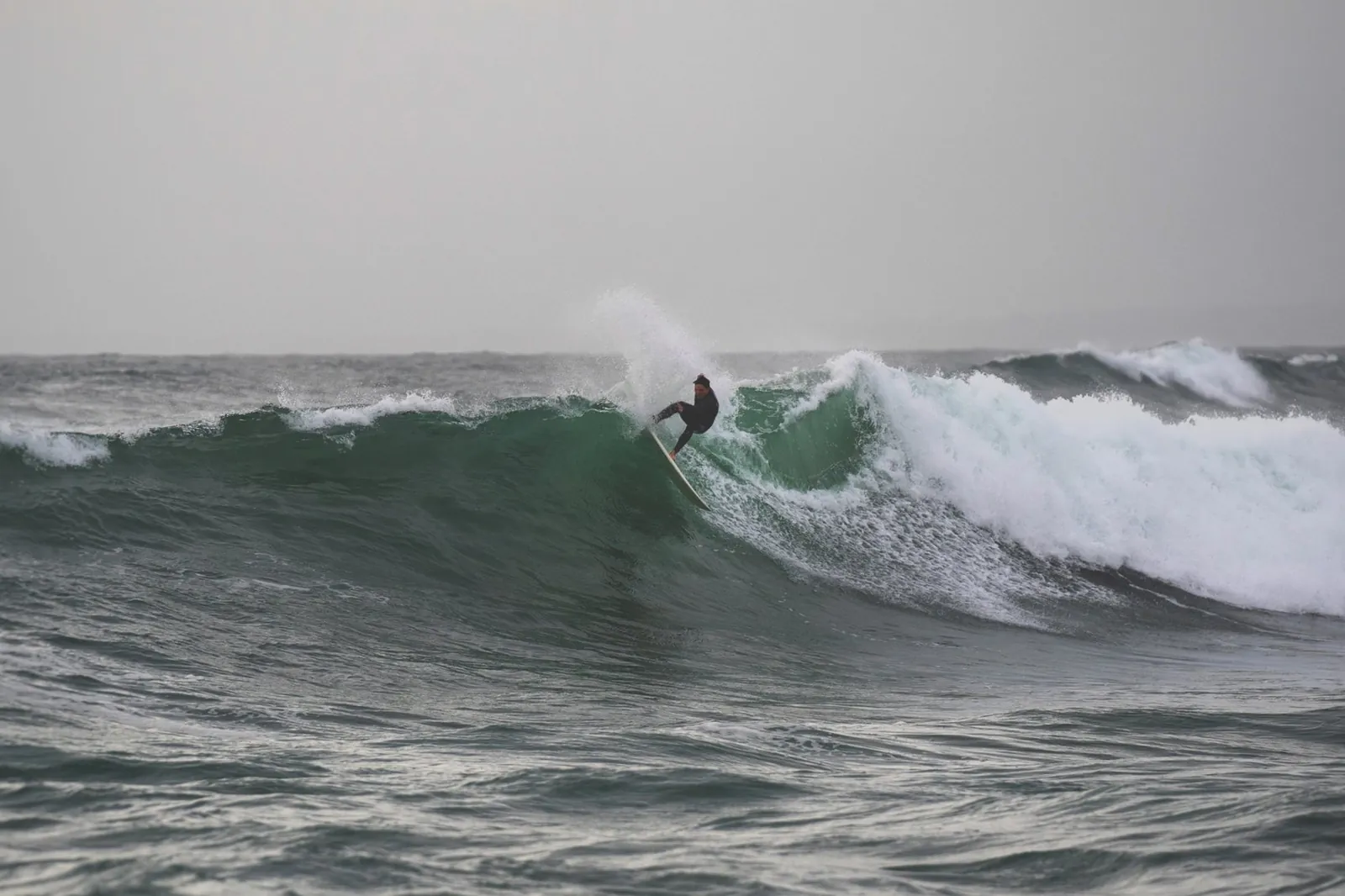 Surfeur en pleine manœuvre sur une vague par temps gris